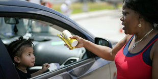 Eine Frau reicht Babynahrung in ein Auto wo ein Kind aus dem Fenster schaut