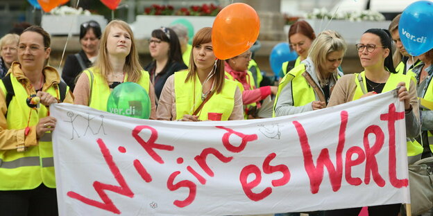 Menschen in gelben Westen mit Verdi-Ballons und einem Plakat "Wir sind es wert"