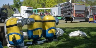 3 Minionfiguren im Vordergrund, Aufbau von Fahrgeschäften im Hintergrund