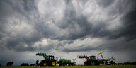 Landwirte verladen Heuballen auf den Anhänger eines Traktors. Hinter ihnen zieht eine Gewitterfront auf