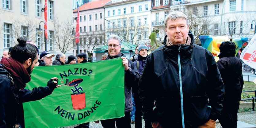 Ein Mann steht vor einem Transparent und blickt in die Kamera