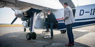 Niedersachsens Ministerpräsident Stefan Weil (SPD) steigt mit Maske aus einem kleinen Privatflugzeug am Flugplatz auf Wangerooge; rechts steht Niedersachsens Umweltminister Olaf Lies (SPD), ebenfalls mit Maske