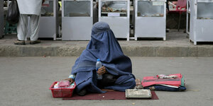Eine verhüllte Frau sitzt auf der Straße und hält eine Wasserflasche in der Hand