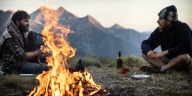 Zwei Männer unterhalten sich am Lagerfeuer vor Bergkulisse