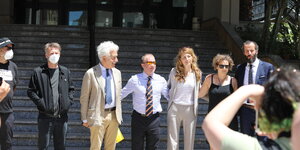Mehrere Menschen, darunter vier Seenotretter:innen und ihre Anwälte stehen vor dem Gericht Arm in Arm nebeneinander