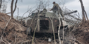 Ein Panzer im Unterholz, auf ihm ein Soldat, der Äste auf den Panzer legt