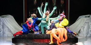 Eine Gruppe Schauspieler*innen in bunten Kostümen auf einer Bühne