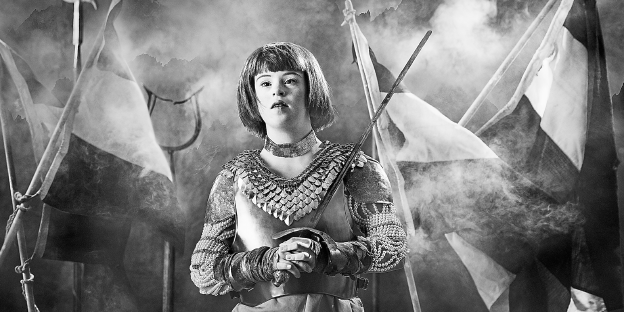 Schwarz-weiß Foto einer jungen Frau mit Trisomie 21, die als Jeanne d'Arc posiert