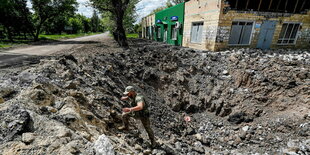 Ein ukrainischer Soldat klettert in einem großen steinigen Loch über Steine