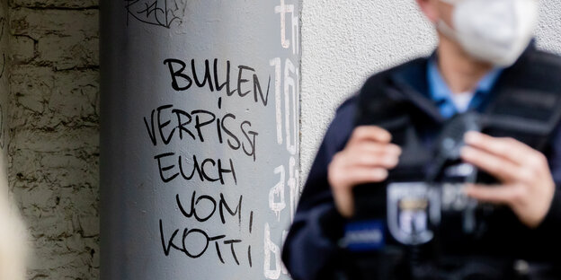 Auf einer Häuserwand am Kottbusser steht mit Edding geschrieben: "Bullen verpisst euch vom Kotti", davor ein unscharfer Polizist