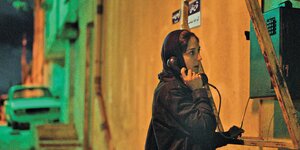 Eine dunkelhaarige Frau mit Kopftuch telefoniert an einer Telefonzelle