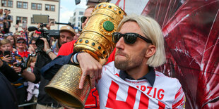 Der Fußballer Kevin Kampl trägt den DFB-Pokal in seinem Arm. Hinter ihm sind viele Menschen. Kampl trägt ein Trikot und eine Sonnenbrille.