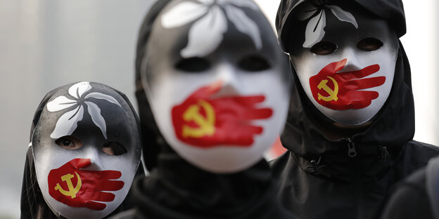 Demonstranten tragen Masken, auf denen eine rote Hand mit chinesischer Flagge abgebildet ist, die den Mund zuhält