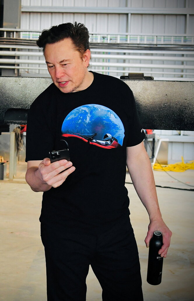 Elon Musk steht in T-Shirt in einer Halle. Auf dem Shirt ist ein Weltraum-Motiv.