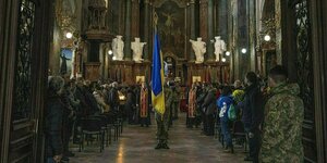 Der Sarg eines Soldaten wird aus der prchtvollen Kirche St. Peter und Paul in Lviv getragen, ein Soldat steht mt der ukrainischen Fahne davor
