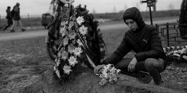Ein Junge legt auf dem Friedhof in Butscha am Stadtrand von Kiew eine Schokolade auf das Grab seines Vaters