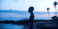 Ein Junge steht an einem spätabendlichen Strand