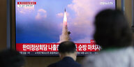 Menscen schauen auf einen Bildschirm, der eine startende nordkoreanische Rakete zeigt