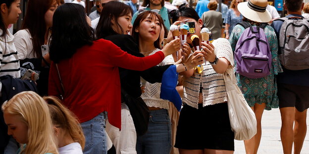 Touristinnen, die sich beim Eisessen fotografieren, drumherum viele andere Touristen