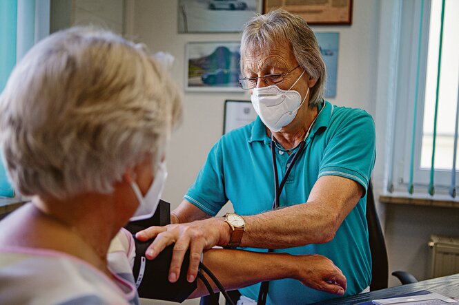 Arzt mit Mundschutz misst Blutdruck bei einer Patientin.