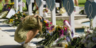 Eine junge Frau hockt vor einer Reihe mit Blumen geschmückter Kreuze