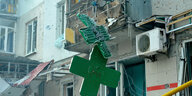 Ein kaputtes grünes Kreuz einer Apotheke, im Hintergrund zerstörte Häuser