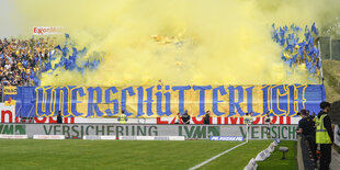 Stadionbanner mit Aufschrift "Unerschütterlich" vor gelbem Rauch