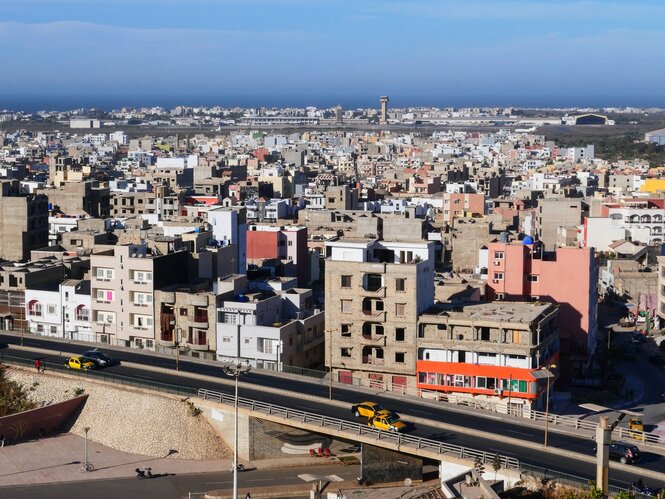 Panorama von Dakar, Autobahn und eher tristes Häusermeer, hinten am Horizont schimmert blau die Atlantikküste