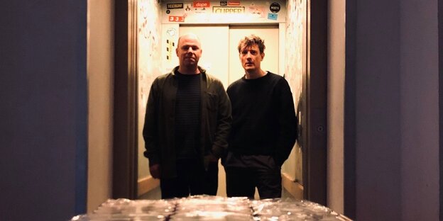 David Grubbs und Jan St. Werner in einer Aufzugkabine, davor eine Pallette mit Dosen