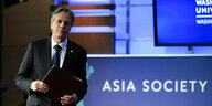 US-Außenminister Blinken vor einer blauen Leuchtwand mit blauen Logos der Asia Society sowie der George Washinton University