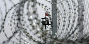 Ein Wachturm mit türkischer Fahne lässt sich durch Ringe von Stacheldraht erblicken.