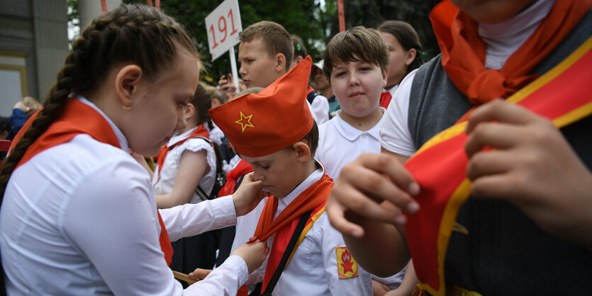 Eine Gruppe von Kindern steht in einer Reihe. Im Vordergrund bindet ein Mädchen einem Jungen ein Halstuch zurecht