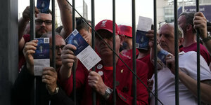 Fans zeigen ihre Eintrittskarten hinter einem Gitter.