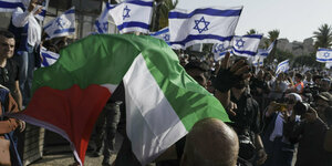 Ein Mann lässt eine palästinensische Fahne vor eienr Gruppe Menschen mit israelischen Fahnen wehen