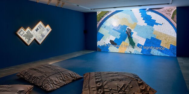 In einem blauen Raum mit Kissen auf dem Boden wird ein abstraktes Video an die Wand projiziert