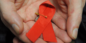 Eine Hand in der eine rote Schleife als Symbol der Solidarität mit Aids-Kranken liegt.
