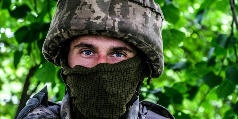 Eine Frau schiebt ein Kleinkind im Kinderwagen, hinter ihr steht ein Soldat in Uniform