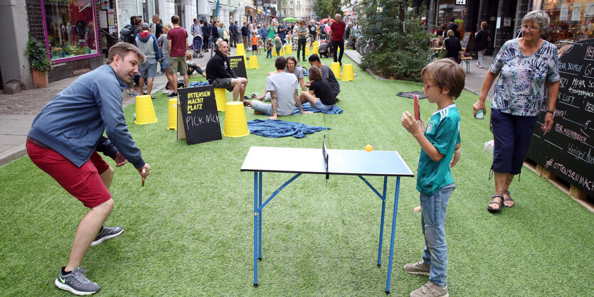 Ein Mann und ein Junge spielen Tischtennis auf künstlichem Rasen, der in einer Wohnstraße ausgelegt ist