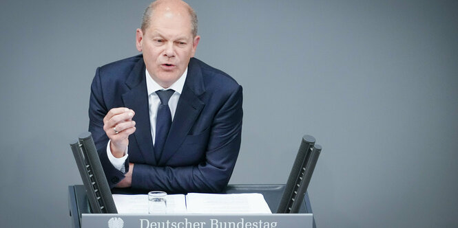 Scholz lehnt auf dem Redepult und gestikuliert