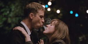 Ein Mann und eine Frau haben sich umarmt, mit geschürzten Lippen tauschen sie Rauch aus