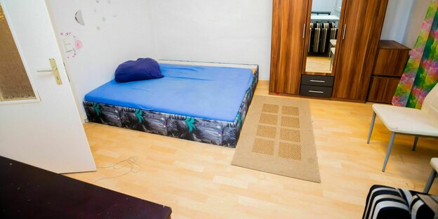 Eine Matraze liegt auf dem Boden in einem spärlich möbilierten Zimmerr