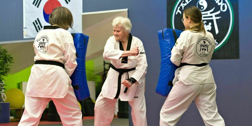 Drei Frauen in weißen Taekwondo-Anzügen trainieren auf einer Matte im Studio