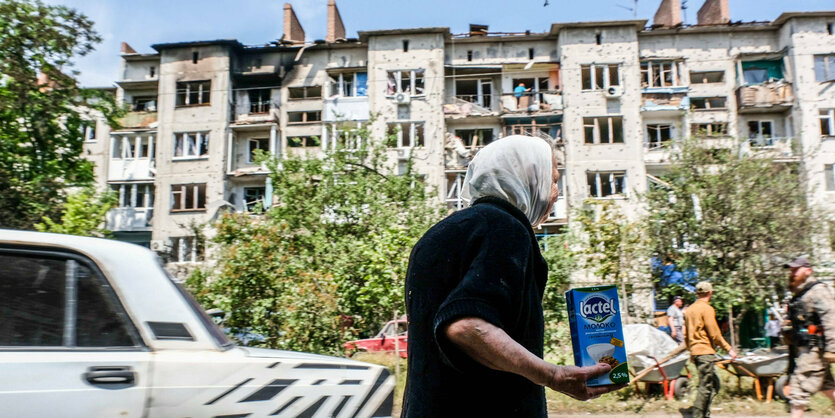 Alte Frau vor beschädigtem Wohnhaus