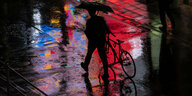 Mann schiebt Rad durch die regnerische Nacht