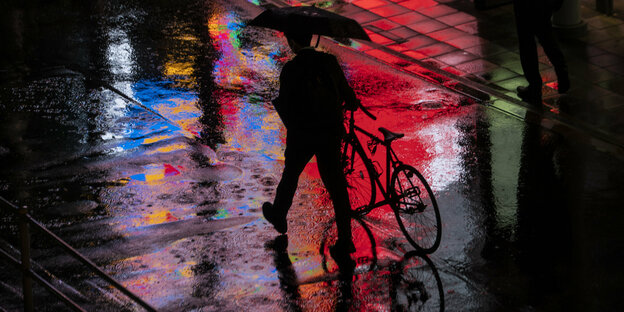 Mann schiebt Rad durch die regnerische Nacht