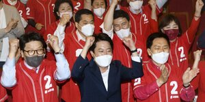 Koreaner in roten Arbeitskitteln und mit Schutzmasken jubeln vor der Kamera.