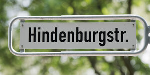 Ein Straßenschild mit dem Schriftzug Hindenburgstraße vor grünen Blättern.
