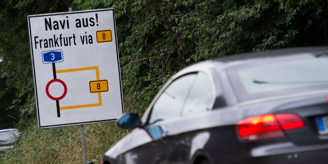 Auto vor einem Hinweisschild, auf dem „Navi aus!“ steht