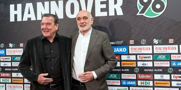 Gerhard Schröder und Martin Kind stehen vor einer Sponsorenwand von Hannover 96