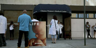 Vor dem Eingang einer Klinik steht ein Protestierender mit dem Bild eines Fötus